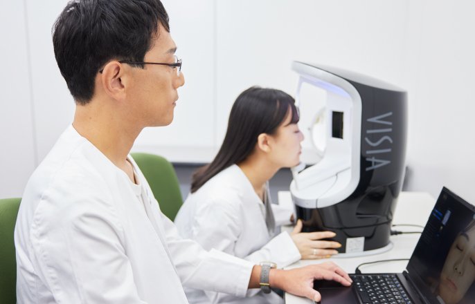 写真：女性が顔を機器に向けていて、立田茂さんが、その女性の顔が映し出されたパソコンの画面を見ている様子