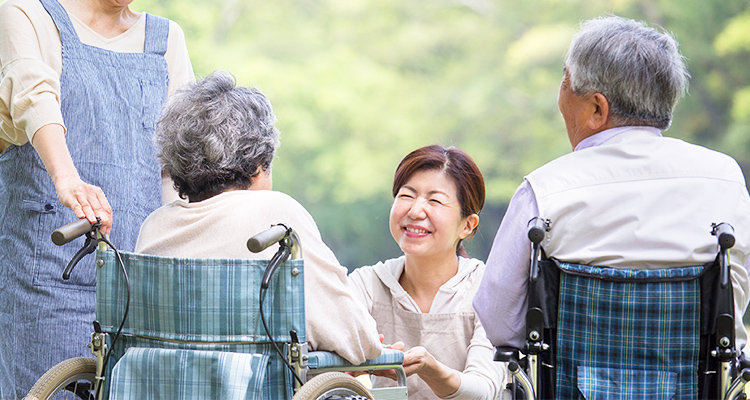 車椅子で公園の散歩に来た老夫婦とご家族の画像です。