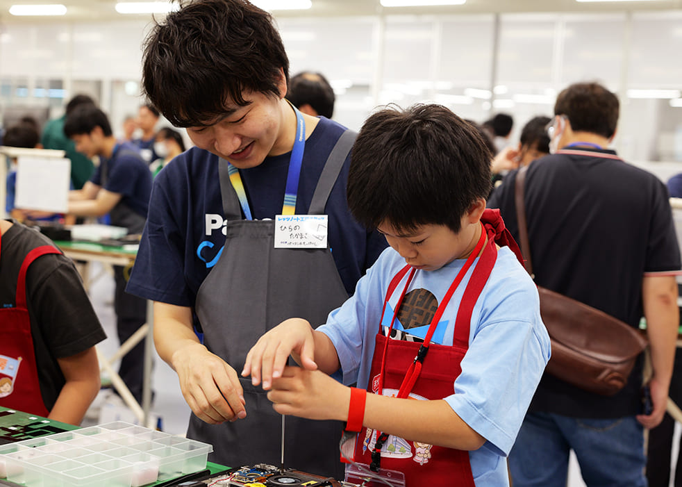 参加者のこどもがエンジニアに教わりながらレッツノートを組み立てている様子