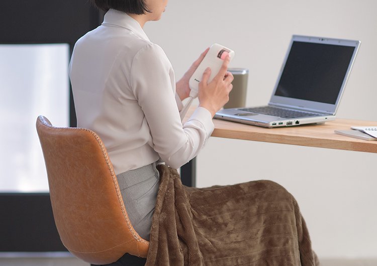 写真：女性が電気ひざかけ くるけっとのコントローラーを操作するイメージ
