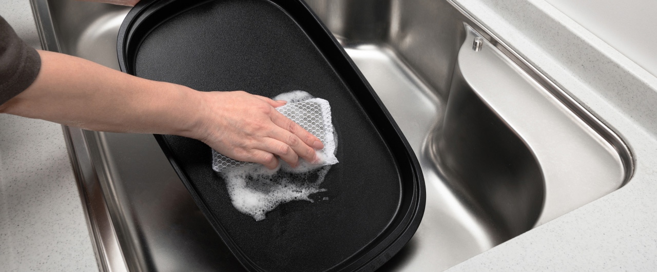 写真：ホットプレートのお手入れ。スポンジで洗うようす。