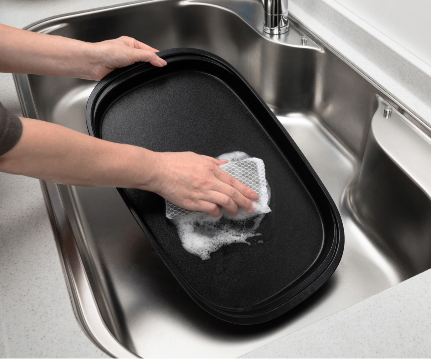 写真：ホットプレートのお手入れ。スポンジで洗うようす。