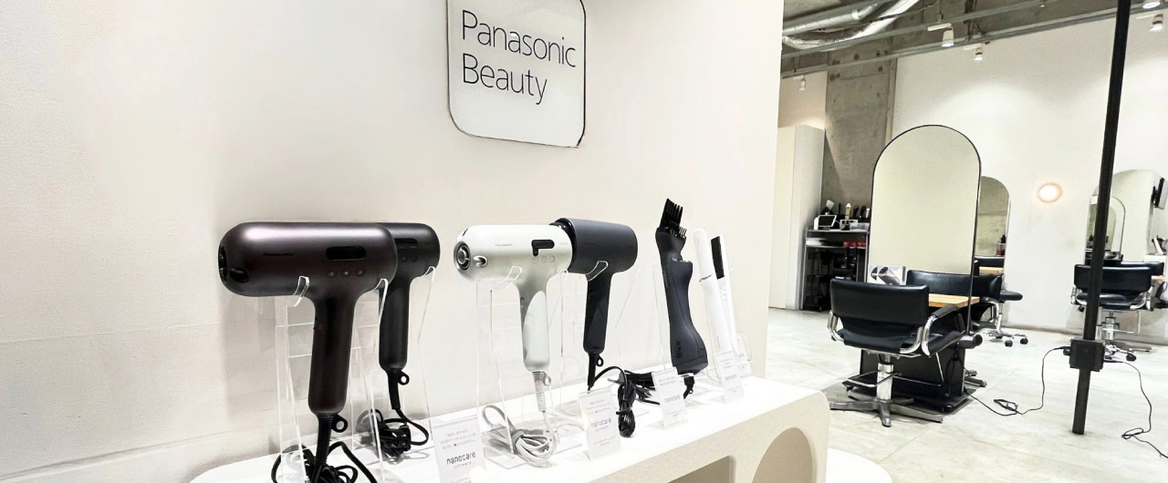 Panasonic Beautyのドライヤーや美容家電が並ぶ展示スペースと、奥にカットチェアやミラーが配置された美容室の内観