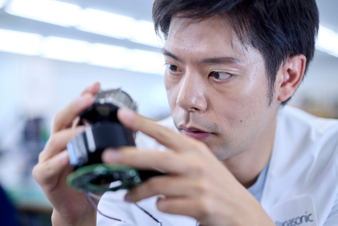 電子機器の部品を手に持ち、細部を確認している前田晃希さん