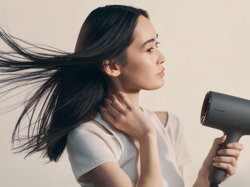 ドライヤーの風で髪をなびかせながらヘアケアをしている女性