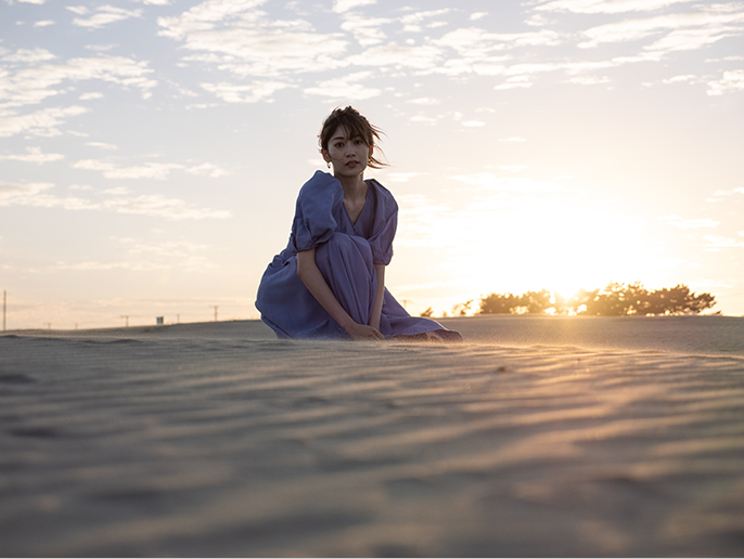 夕日を背に受けて砂の上に座る女性