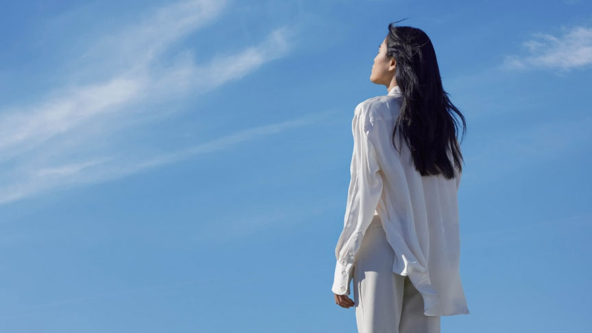 青空に目線をあげる女性の後ろ姿