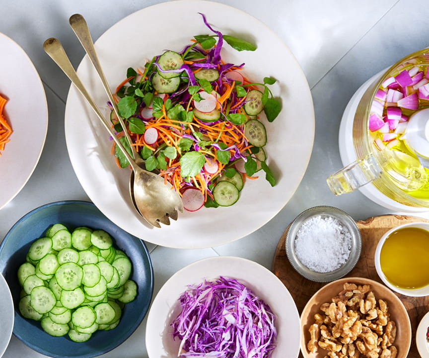 写真：細切りにされた野菜やサラダ、ナッツ、調味料などと、フードプロセッサーが並んだ食卓