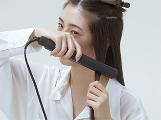 写真:［1］コンパクトストレートアイロンで髪をはさんでいる女性の様子