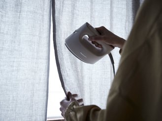 ［写真］衣類スチーマーでカーテンをケアしている様子