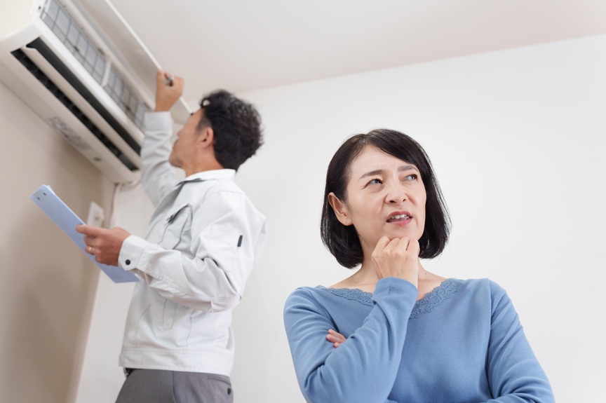 写真：エアコンを点検する男性と困り顔の女性