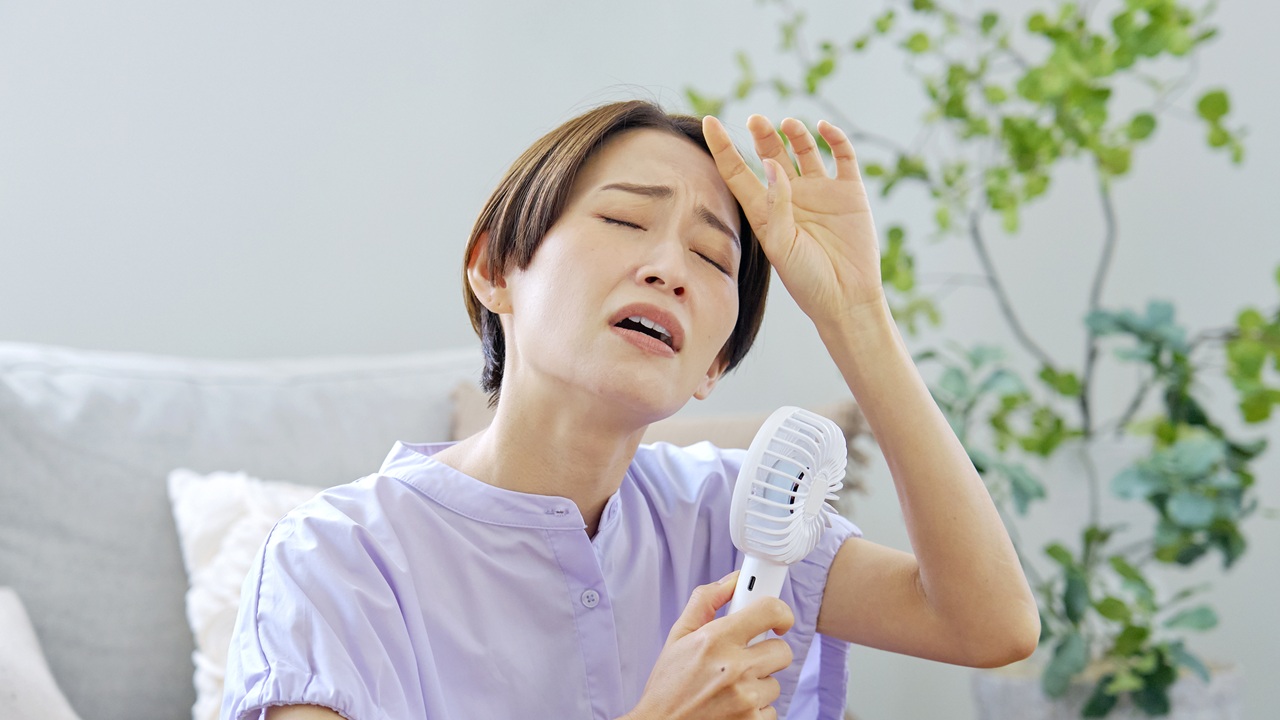 ハンディファンを使っている暑そうな女性の写真
