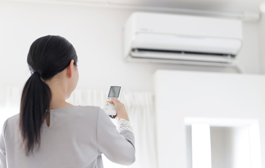 写真：エアコンのスイッチを入れる女性のイメージ