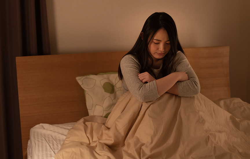 写真：ベッドに座り、掛け布団を抱えている女性