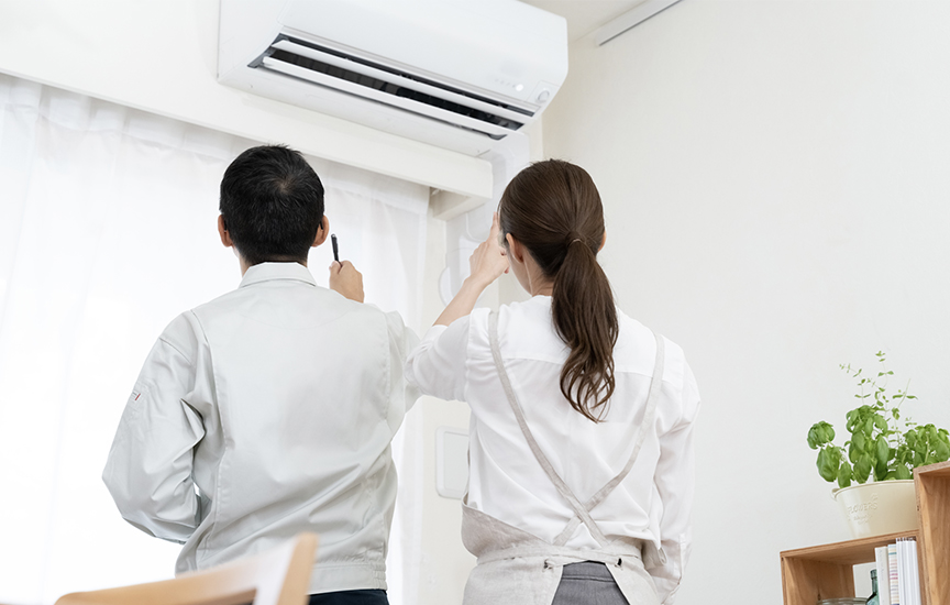 写真：修理業者と一緒にエアコンを見つめる女性