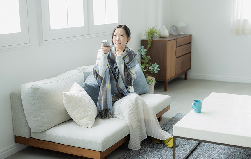 写真：エアコンのリモコンを操作する女性