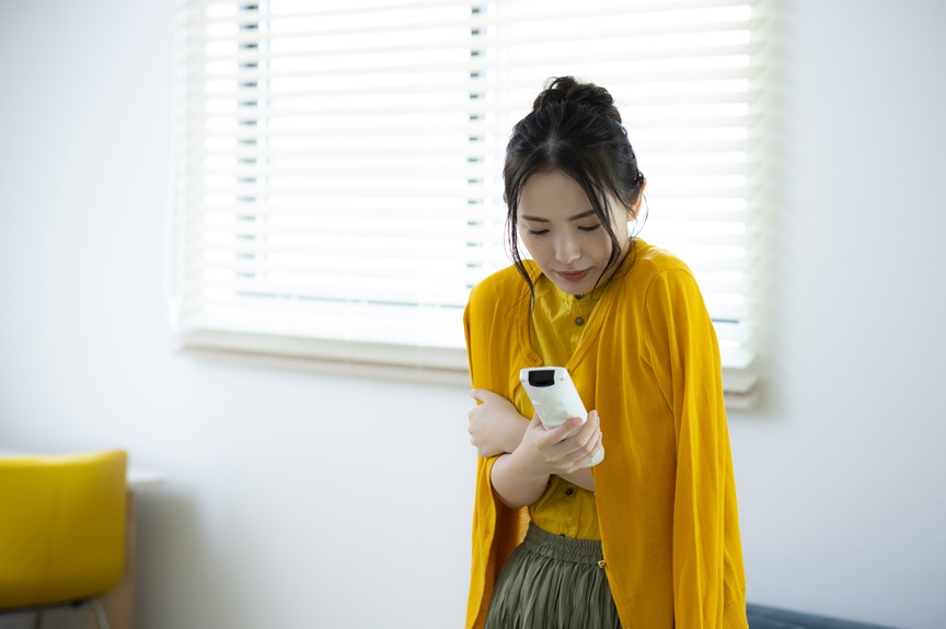 写真：寒がりながらエアコンを操作しようとしている女性