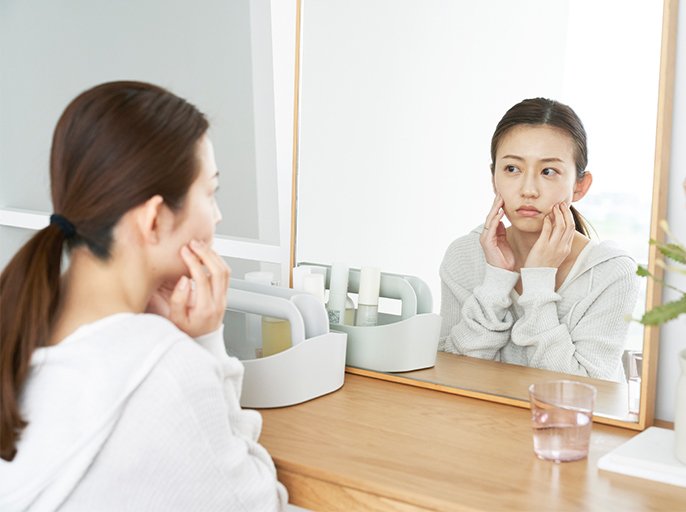 写真：不安そうな表情で鏡にうつる自分を見てる女性