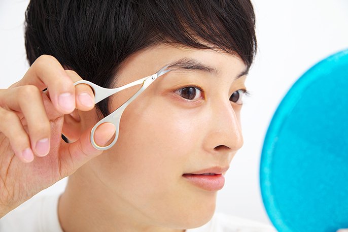 鏡を見ながら眉毛を整えている男性の写真