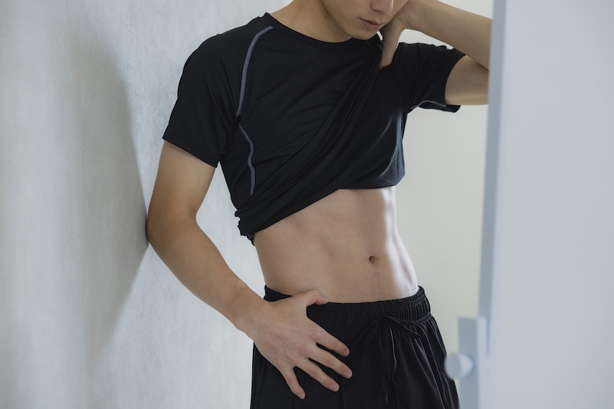 服をまくり上げてお腹を見せている男性の写真