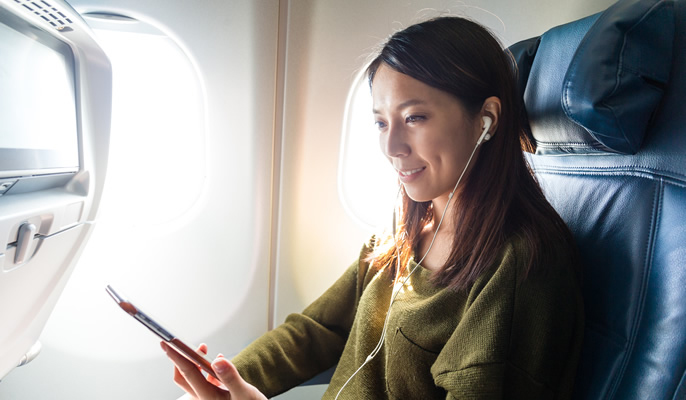 女性が機内でイヤホンをつけてスマホで番組を視聴している様子の写真