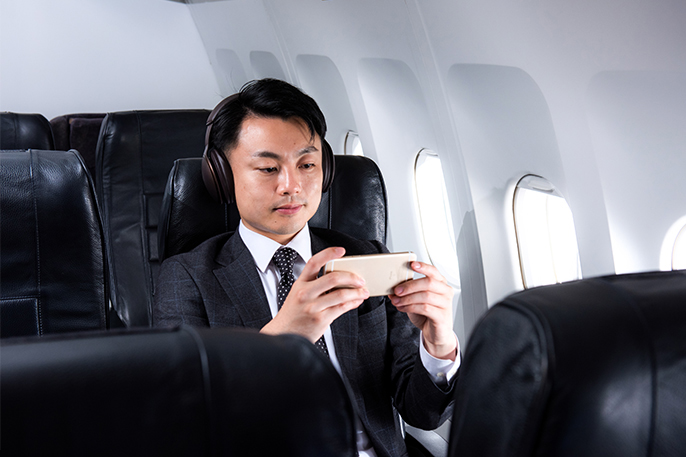 写真：男性が飛行機内でヘッドホンを装着しながらスマホで何かを視聴している様子