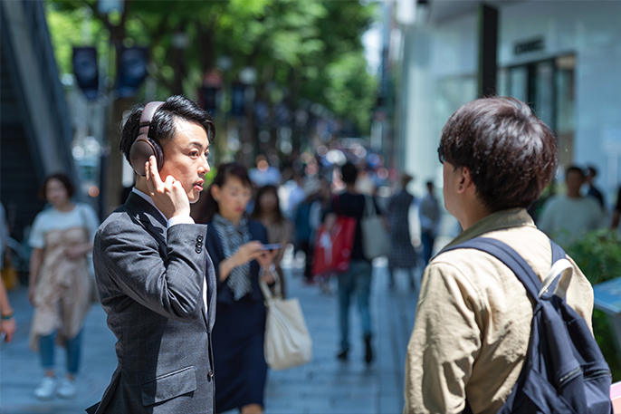 写真：男性が街中で装着しているヘッドホンを触っている様子