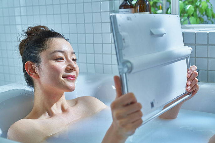 写真：小型テレビを持って浴槽に浸かる女性