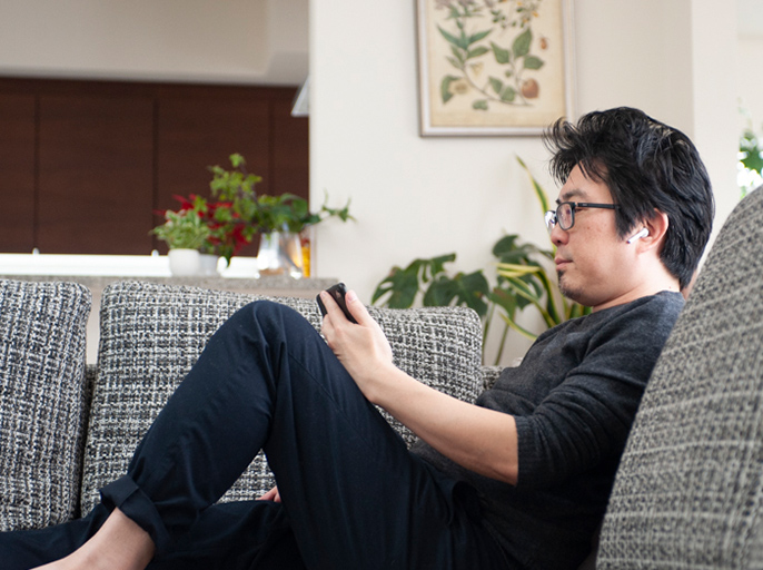 ソファに腰かけてスマホでテレビを見ている男性の写真