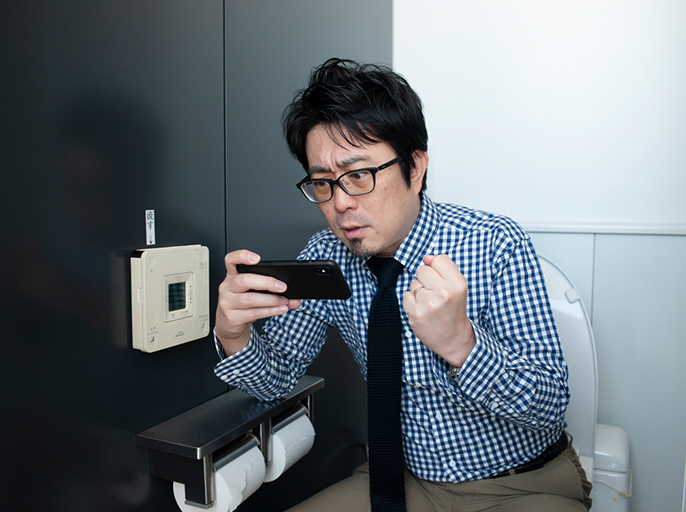 写真:トイレでスマホを見ながらガッツポーズをする松井謙介さん