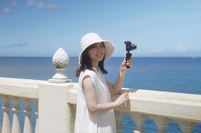 写真：海が見える場所で女性がカメラ持っているイメージ
