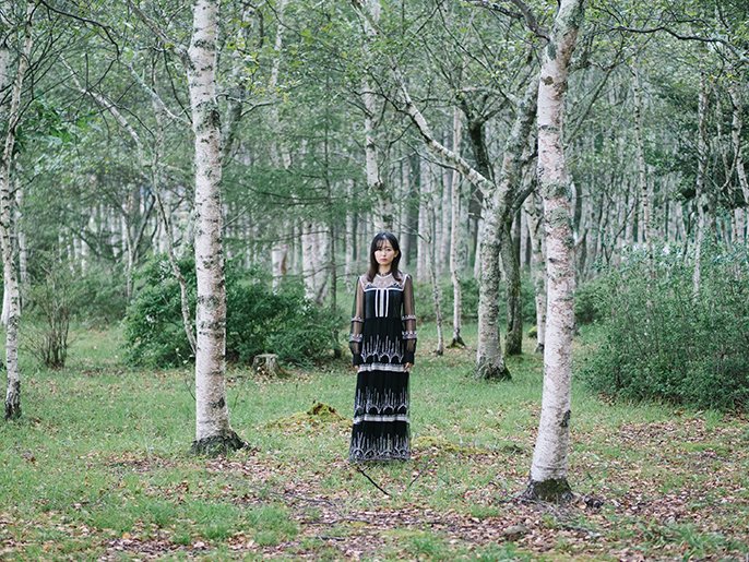 写真：林の中に立つワンピースを着た女性