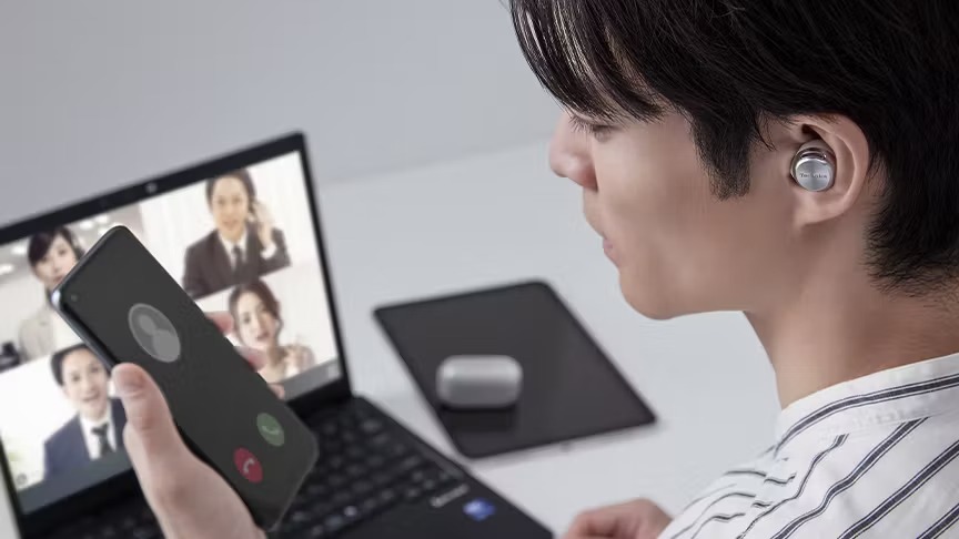 ノイズキャンセリングイヤホンを装着してオンライン会議とスマートフォン通話を行う男性の写真