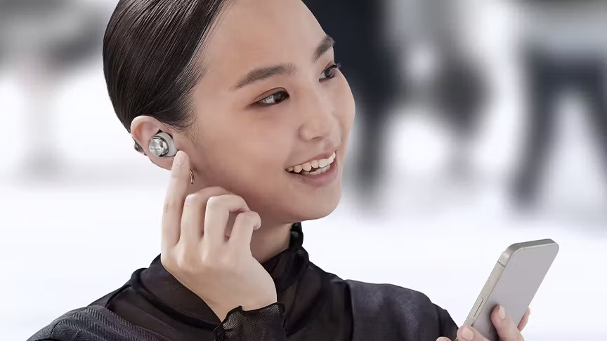 スマートフォンを手に持ちワイヤレスイヤホンに触れる女性の写真