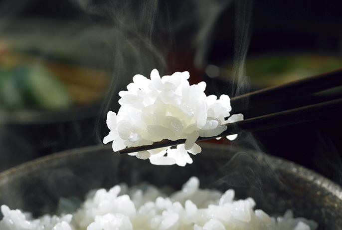 湯気の立つご飯を箸で持ち上げている写真