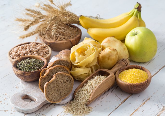 写真：バナナや梨、芋類、パスタ、穀物類がテーブルに並べられてるイメージ