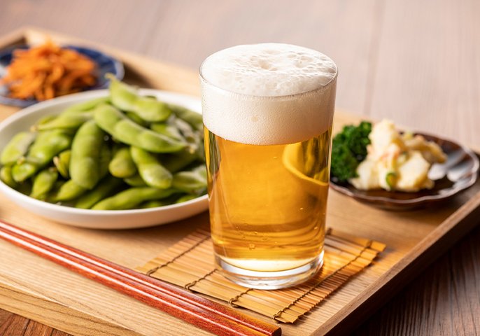 写真：グラスに注がれたビールと枝豆となどのおつまみが並んでいるイメージ