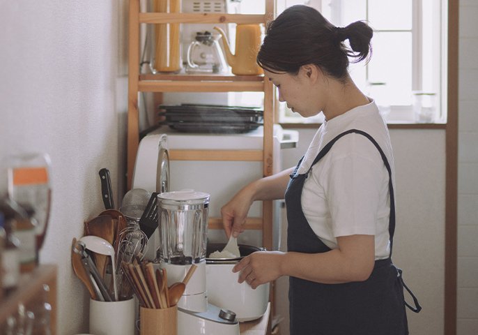 写真：女性がキッチンで炊きあがったご飯を混ぜているイメージ