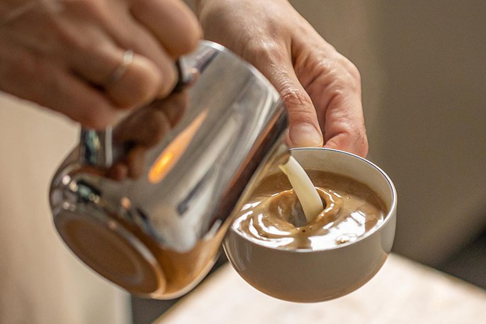 写真：エスプレッソコーヒーに、スチームミルク（蒸気で温めたミルク）を注いでるイメージ