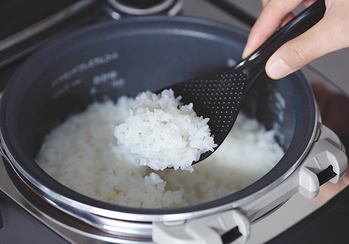炊飯器から炊きあがったご飯をすくいあげてるイメージの写真