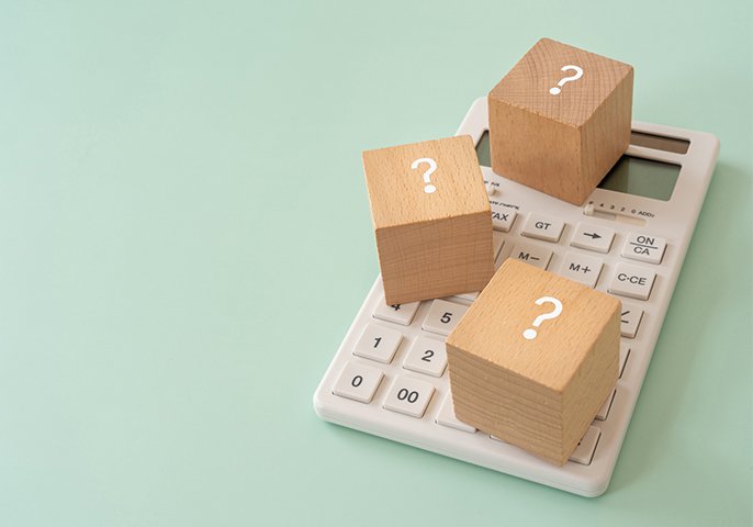 写真：電卓の上に、？と書かれた木製の正方形ブロックが3つ置かれている