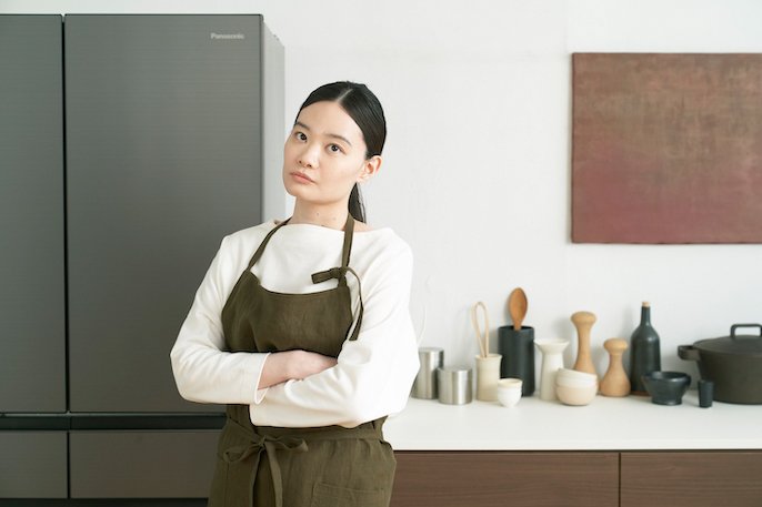 写真：冷蔵庫の前に立った女性が、腕を組んで、首をかしげている様子