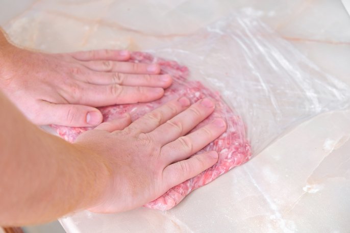 写真：冷凍用保存袋の中に肉を入れ、両手で袋内の空気をしっかり抜いている様子