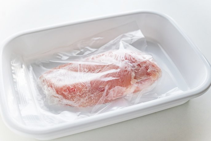 写真：ラップで包まれた鶏肉が入っている冷凍用保存袋が、お皿の上に置かれた様子