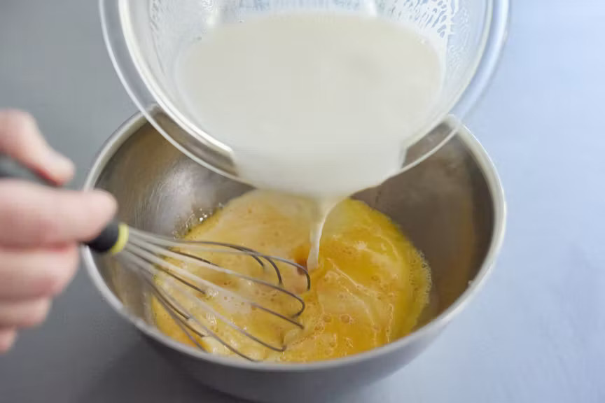 写真：ボウルに卵を入れて溶きほぐし、温めた牛乳を少しずつ入れてよく混ぜる様子
