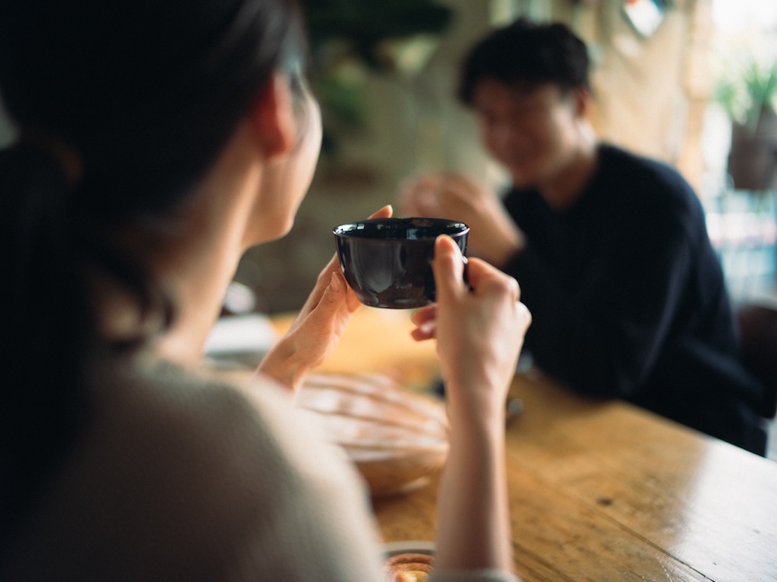 テーブル越しに温かい飲み物を味わいながら談笑する男女の写真