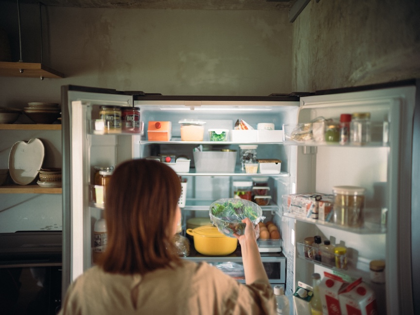 冷蔵庫を開けて中の食品を取ろうとしている女性の写真