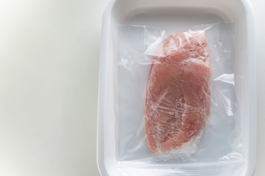 バットの上に置かれたラップとジッパーバッグで保存された鶏肉の写真