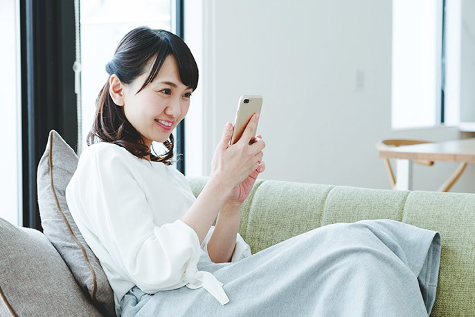 写真：女性がソファでスマートフォンを操作しているイメージ