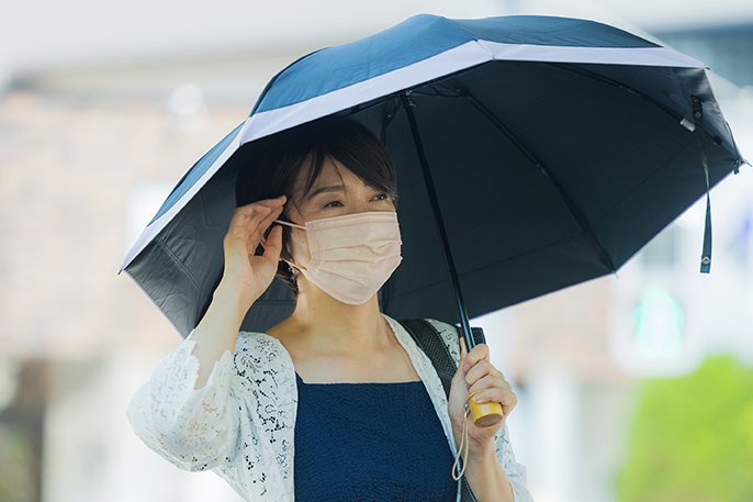 写真：マスクをした女性が傘をさしているイメージ